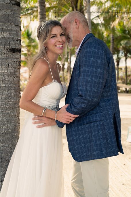 Bride and groom smiling together, embracing near palm trees on a sunny day.