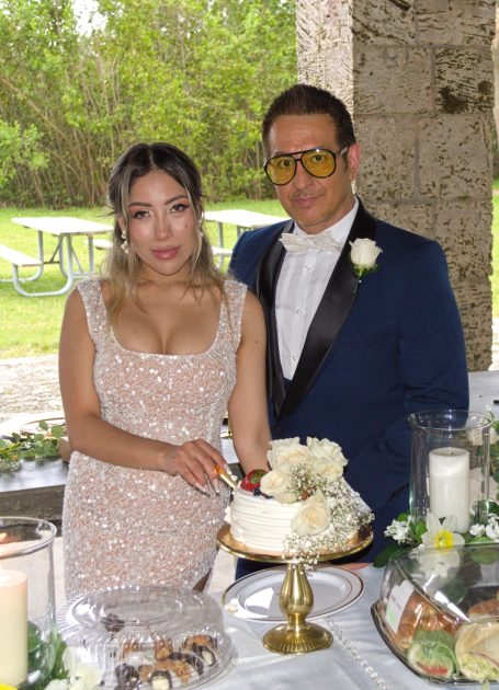 Couple at a wedding, standing beside a decorated cake and table with floral arrangements.