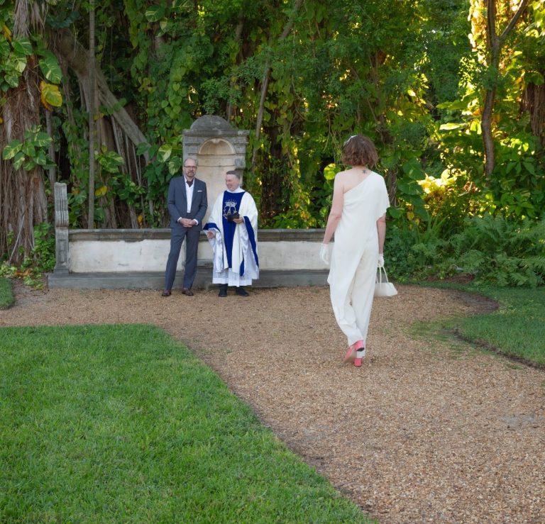A groom in Miami and his brides holds a bouquet of flowers, smiling outdoors.