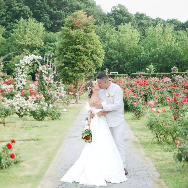 Couple embracing in a rose garden, surrounded by blooming flowers by Iris Ramil Wedding Day Romance