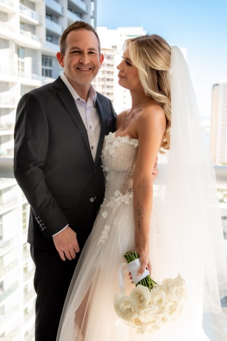 Bride and groom posing together with a cityscape background. The bride holds a bouquet.