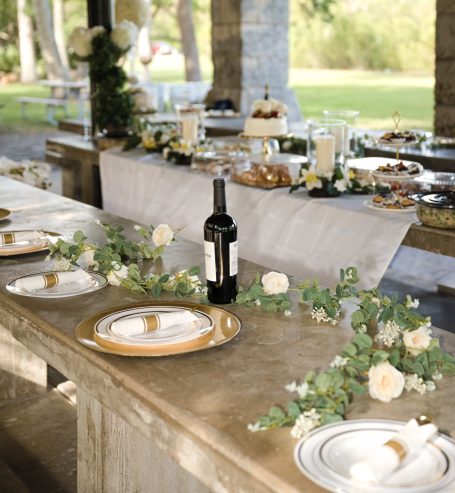 Elegant outdoor dining setup with wine, gold-accented plates, and floral decor.