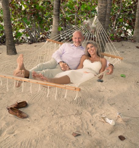 Couple relaxing together in a hammock on the beach, surrounded by greenery.