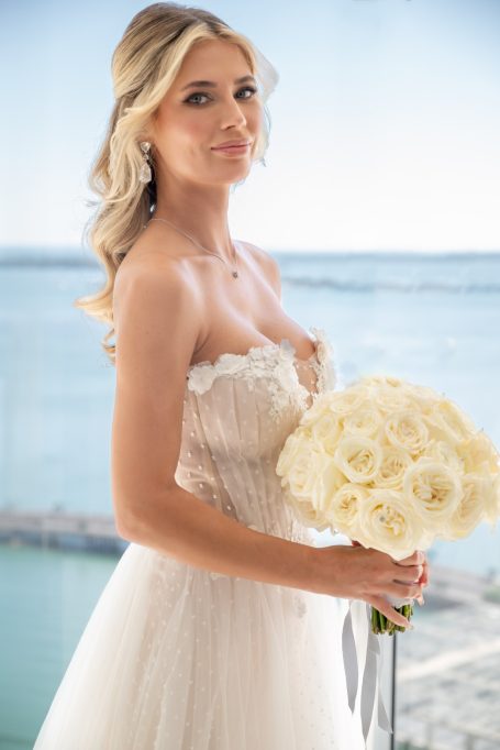 Woman in a wedding dress holding a bouquet of white roses with a seaside background.