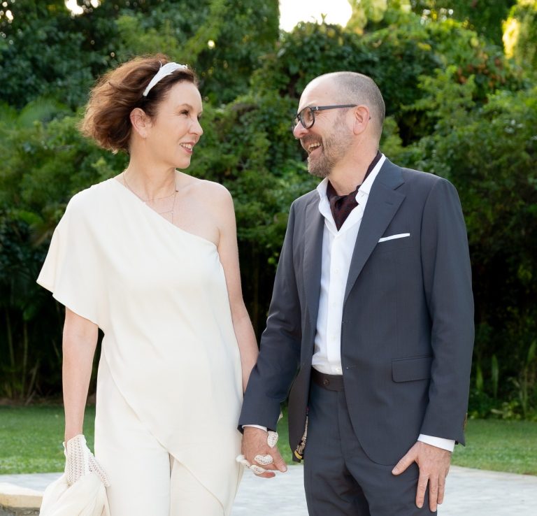 A couple walks hand-in-hand, at The W Hotel, bride in a white gown, beneath tall, dark pillars at The W Hotel
