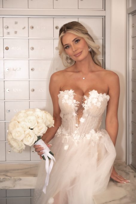 Bride in a floral lace gown holding a bouquet of white roses, smiling softly.