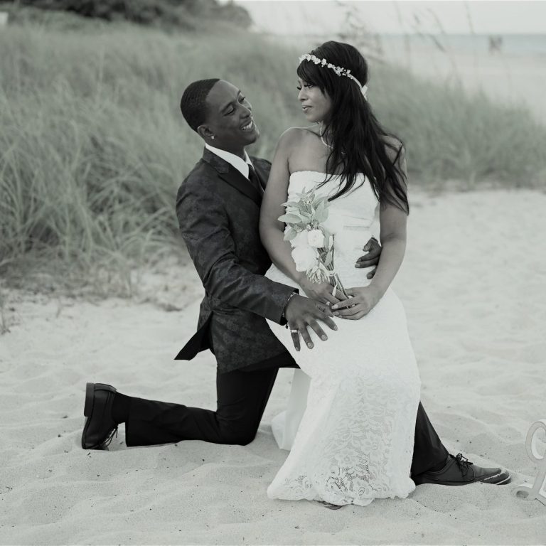 Close-up of bride & groom's hands with wedding rings holding a bouquet of white roses & baby’s breath.
