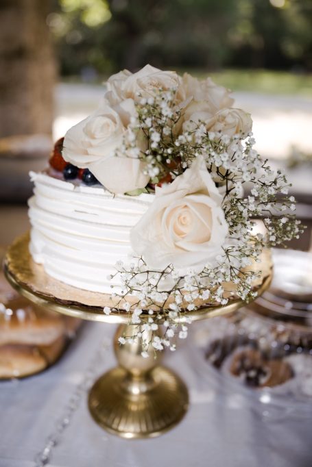 White wedding cake adorned with roses and baby's breath on a decorative stand.