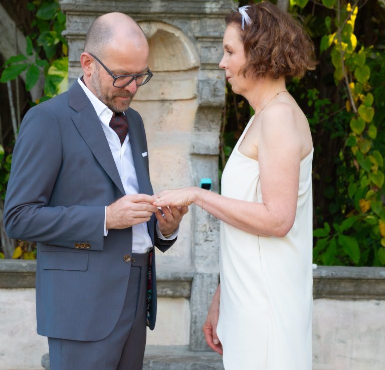 Just married by Iris Ramil wedding officiant, a Bride & groom holds hands, bride with bouquet, walking away.