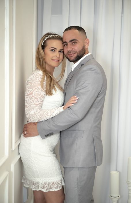 Bride & groom pose together, smiling, in our bright setting with wedding arch in Miami.