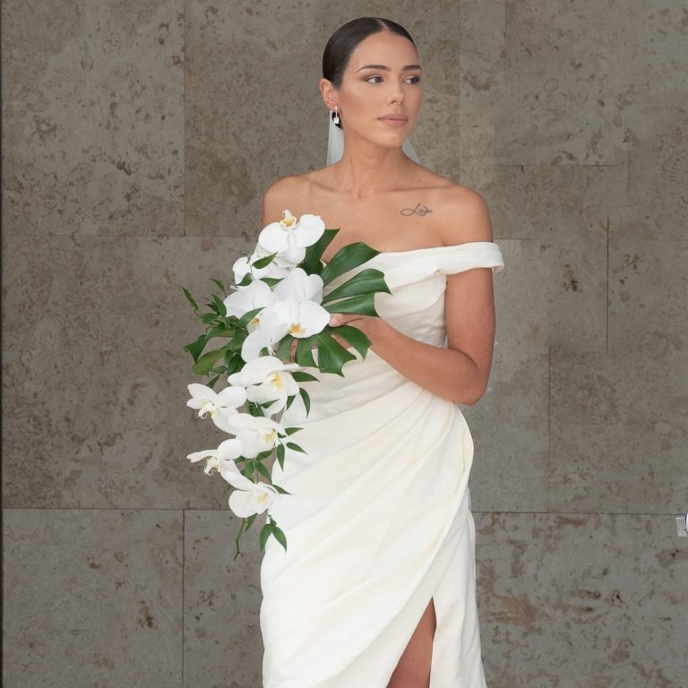 Bride in an elegant off-shoulder white dress, holding a bouquet of white lilies created by Wedding Day Romance