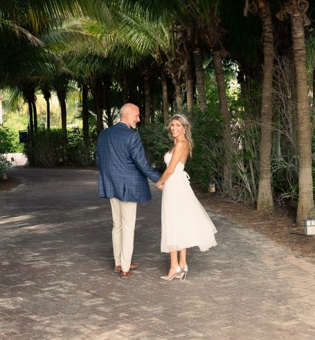A couple dressed for a wedding walks hand in hand down a palm-lined path.