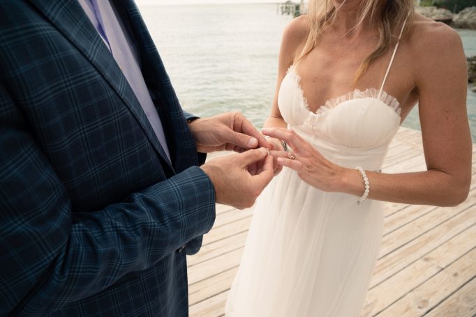 A couple exchanges wedding rings on a dock by the water.