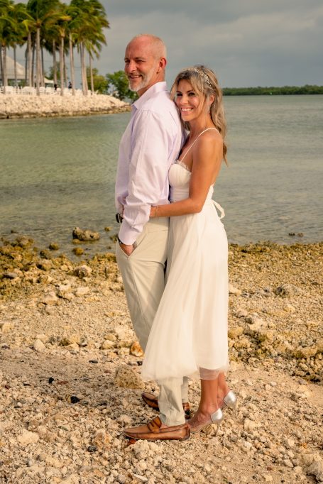 Couple standing by the water on a beach, dressed for a wedding.