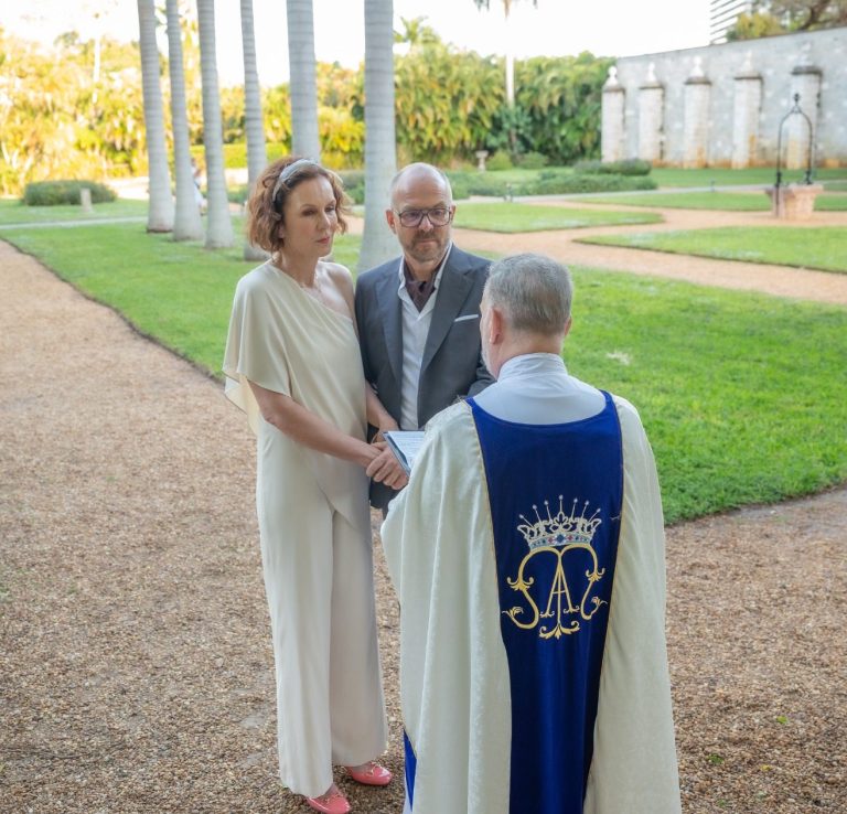 A newly married bride and groom by Iris Ramil wedding officiant with a bouquet in a sunny outdoor setting.