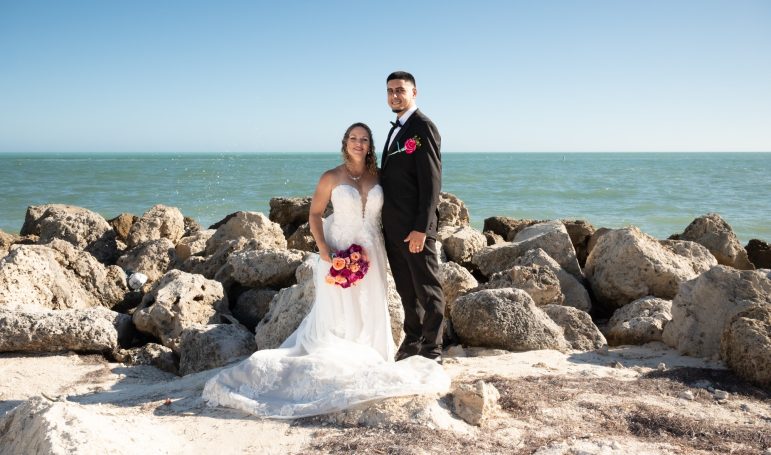 Bride and groom posing on a rocky shoreline with the ocean in the background at Key Largo Florida by Iris Ramil Wedding Officiant.