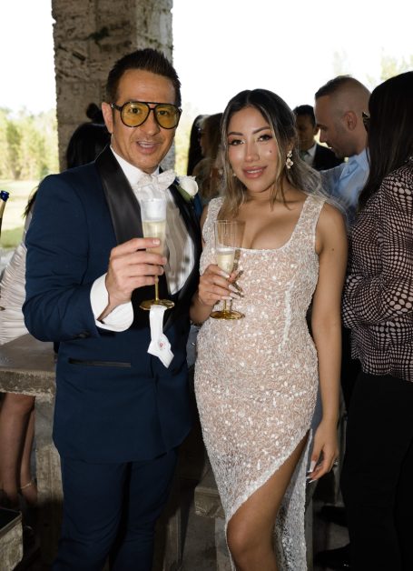 Man in a blue suit and glasses, woman in a sparkling dress, both holding champagne glasses.