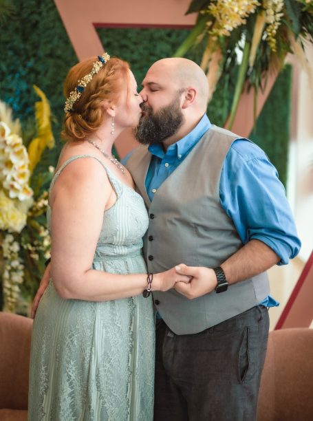 A couple shares a kiss, both smiling, in a decorated indoor setting.