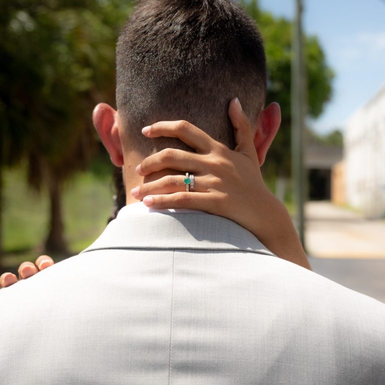 A close-up of groom in a suit with bride's hand embracing him and showing her wedding ring.