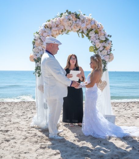 A beach wedding ceremony with a couple exchanging vows under a floral arch.