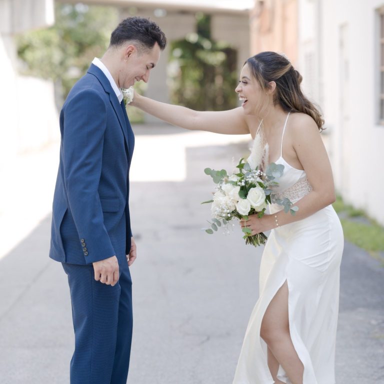 A bride playfully adjusting her groom's tie outdoors at Wedding Day Romance in Pinecrest Florida