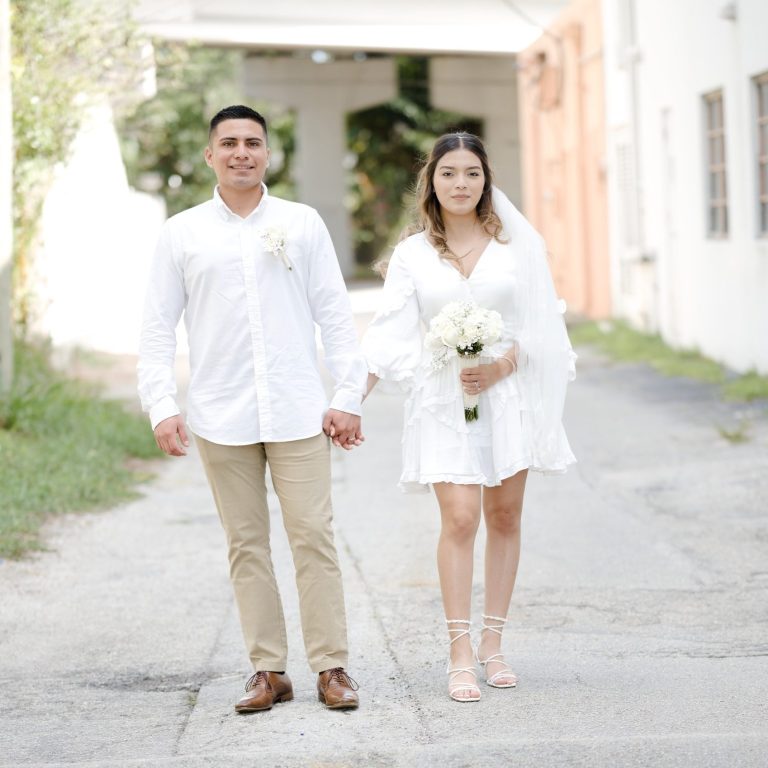 A newly married bride and groom by Iris Ramil wedding officiant with a bouquet in a sunny outdoor setting.