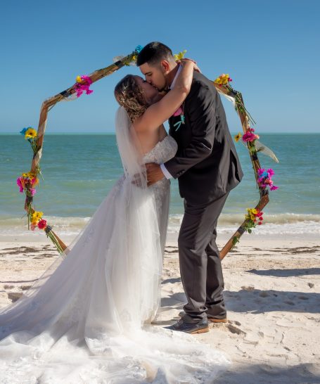 A bride & groom share a kiss under a floral arch in Key Largo Florida by Iris Ramil Wedding Officiant