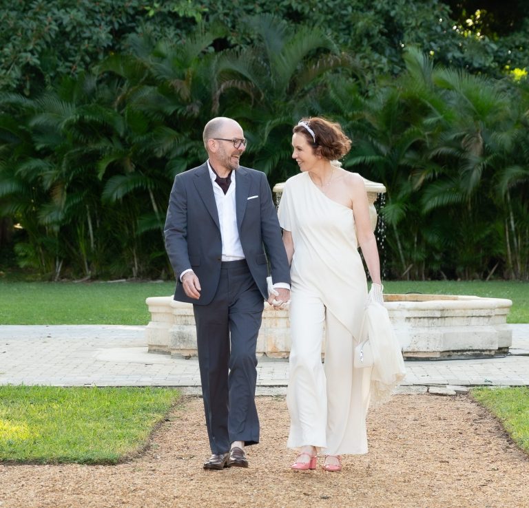 A couple walks hand in hand along a garden path, surrounded by lush greenery.