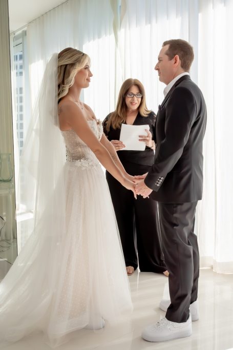 Bride and groom holding hands during their wedding ceremony with a wedding officiant.