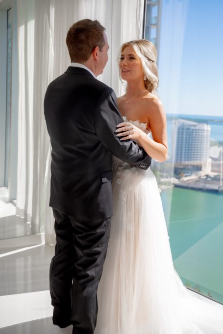A couple embraces, overlooking a scenic waterfront view from a modern high-rise.