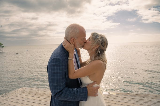 Couple kissing by the ocean, with a cloudy sky in the background.